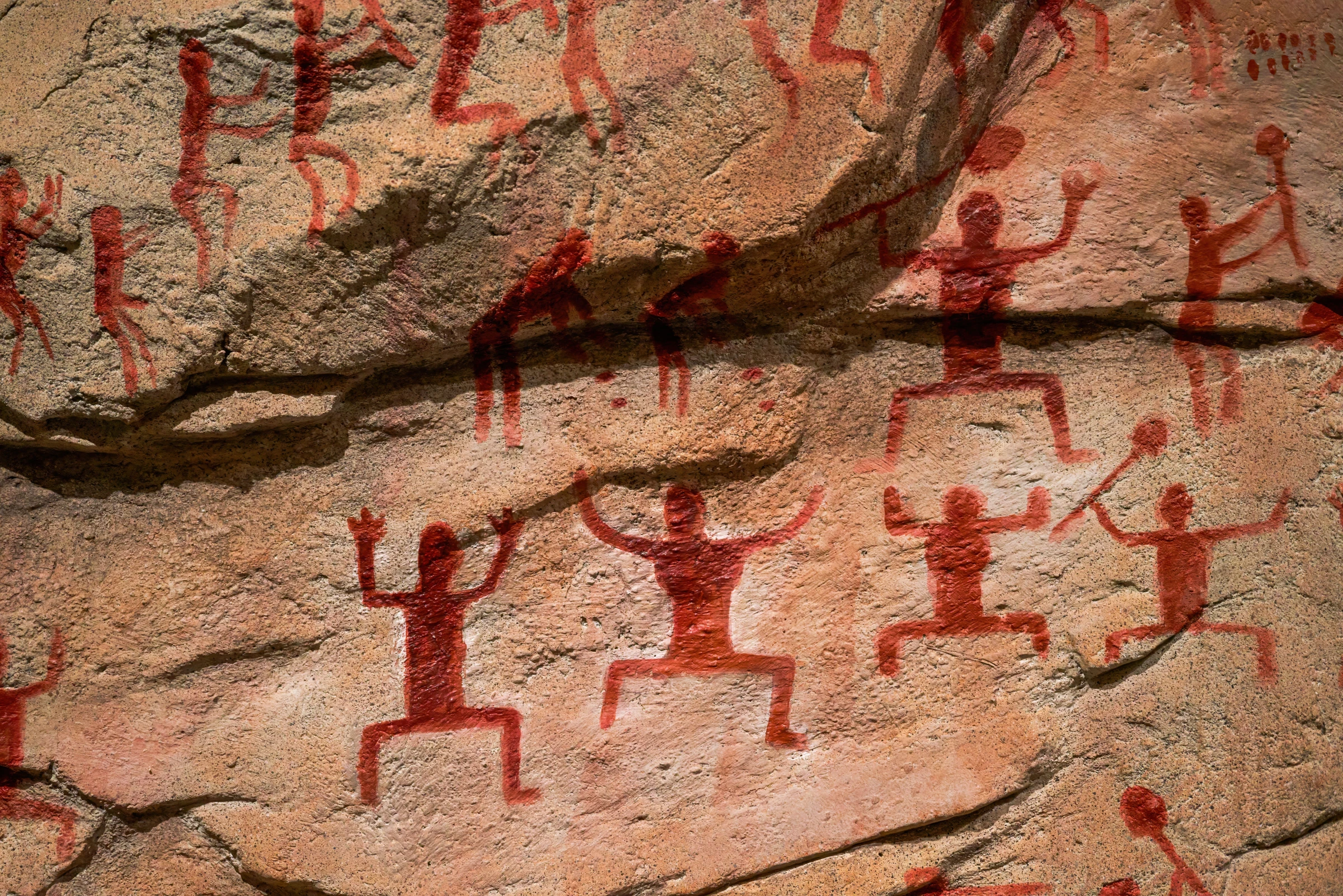 Huashan rock art on karst limestone cliffs in Guangxi, China, showing vivid red figures of people wearing feather headpieces playing drums and bells in what may be an ancient fertility rite