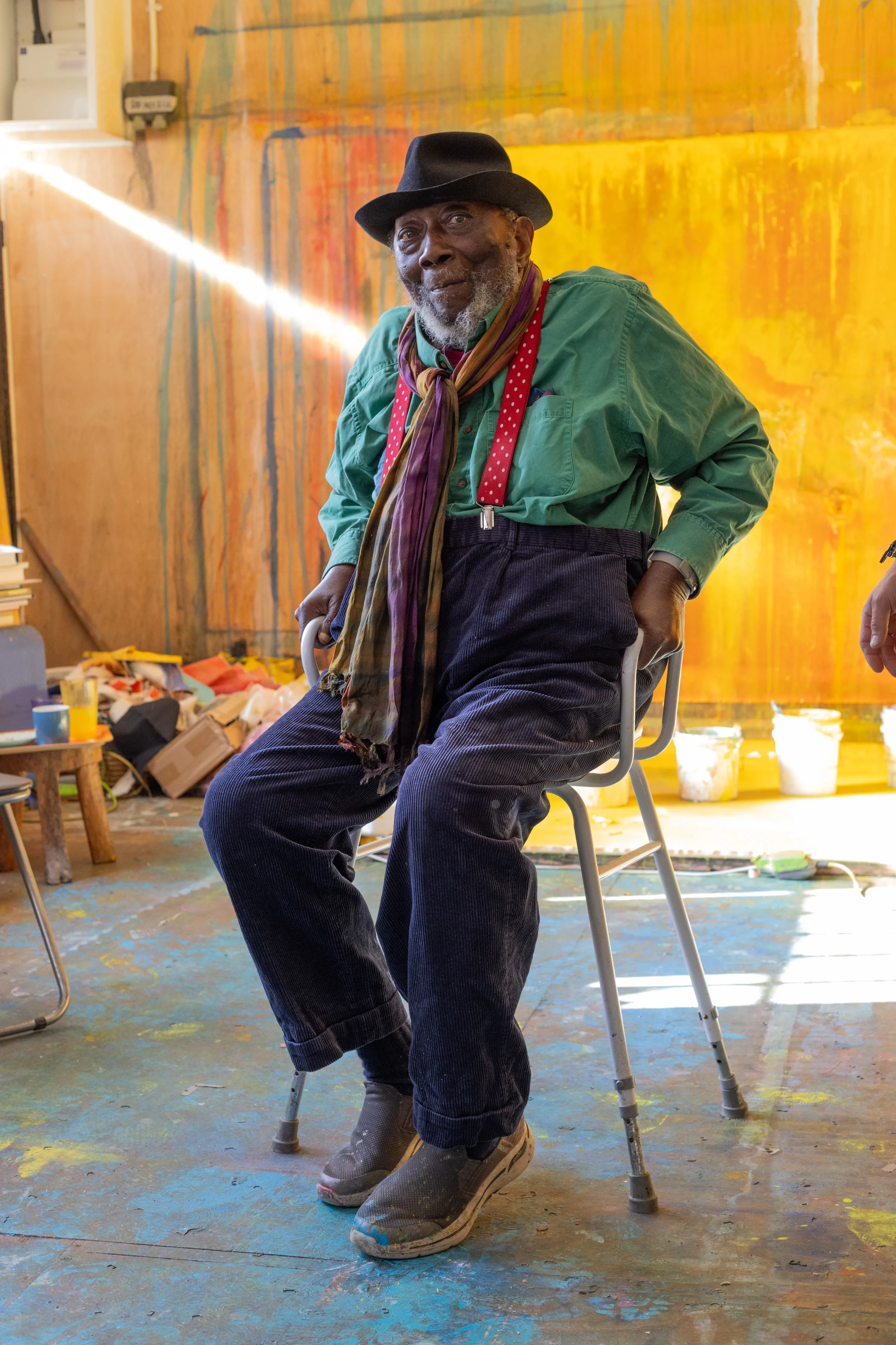 Frank Bowling seated in his studio before a large yellow-orange painting