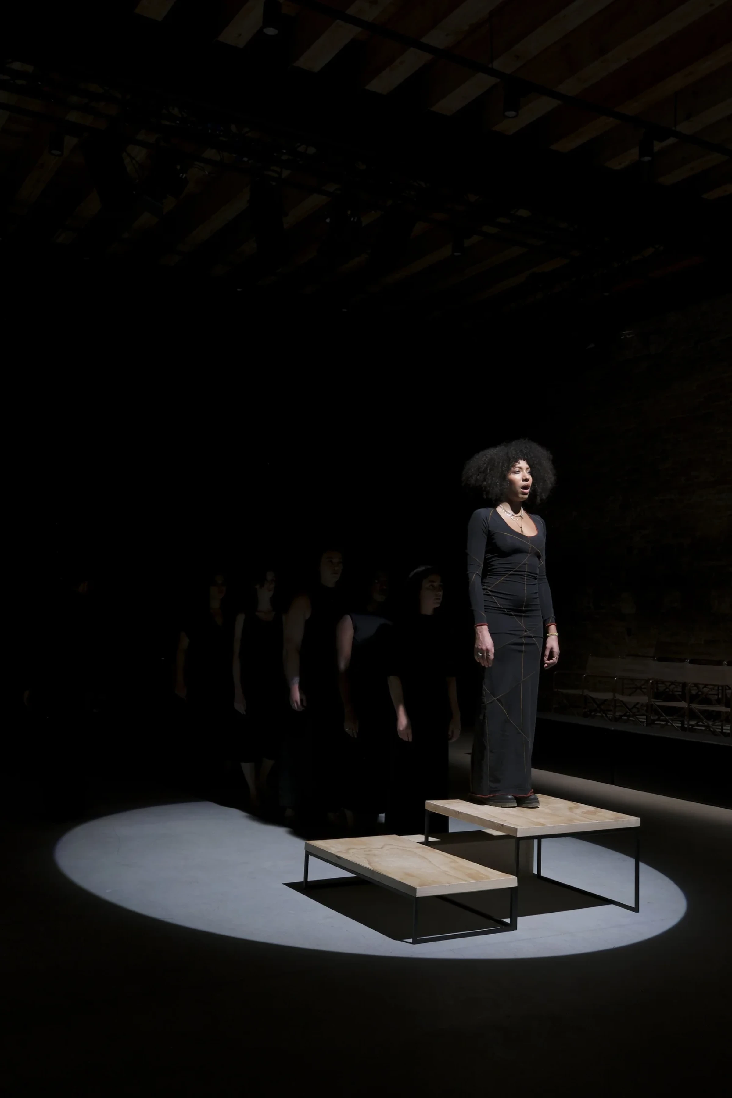 Performance view of Gabrielle Goliath’s Elegy with singers standing in a dimly lit space.