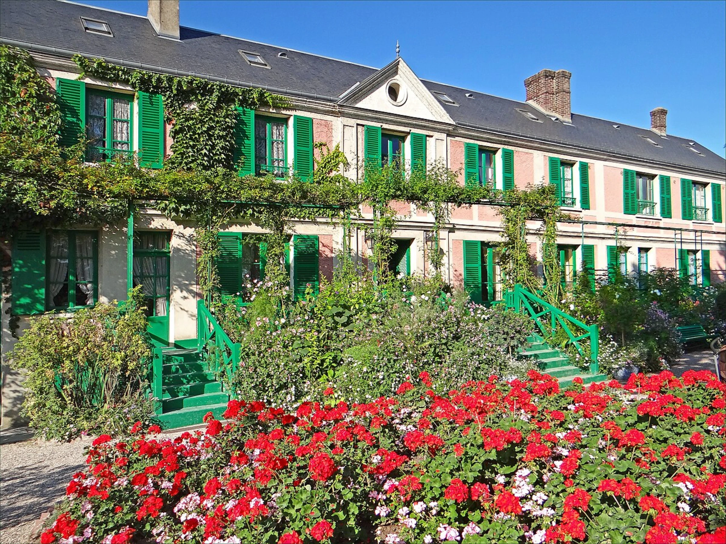 Claude Monet's house and gardens in Giverny, Normandy, with the iconic pink facade and green shutters visible through lush plantings