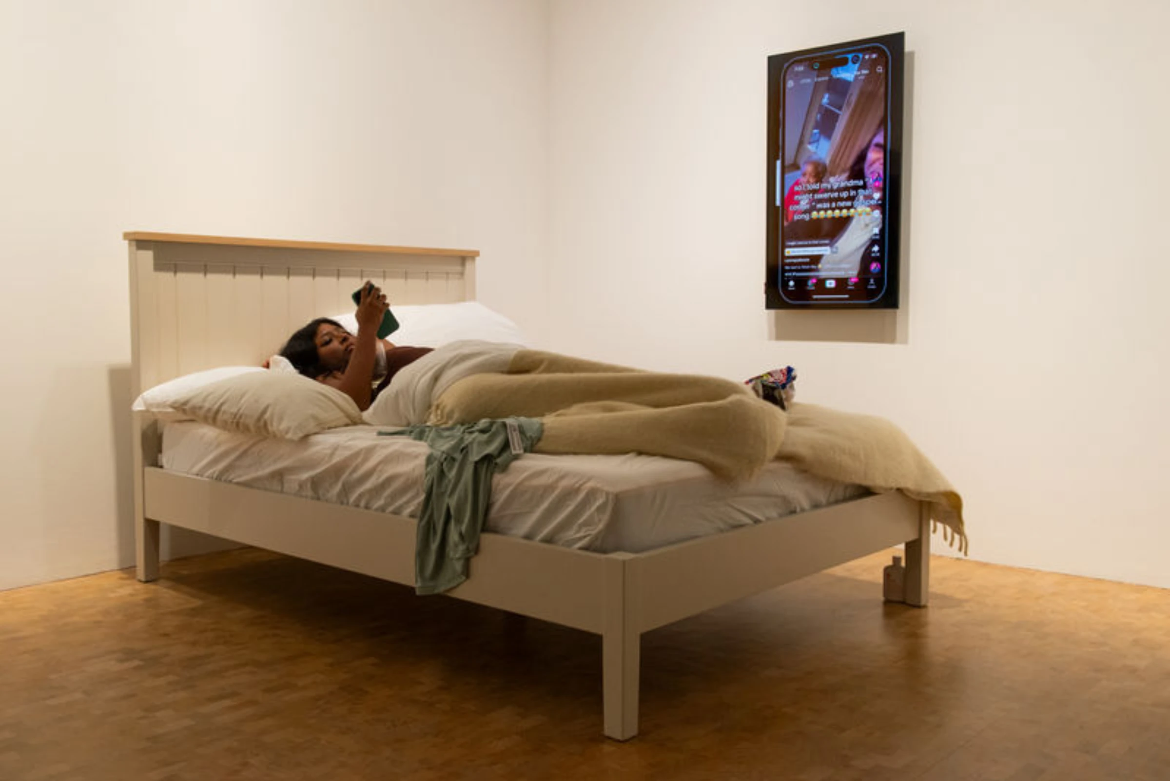 Qualeasha Wood performing from a bed within an installation environment of digital-textile works.